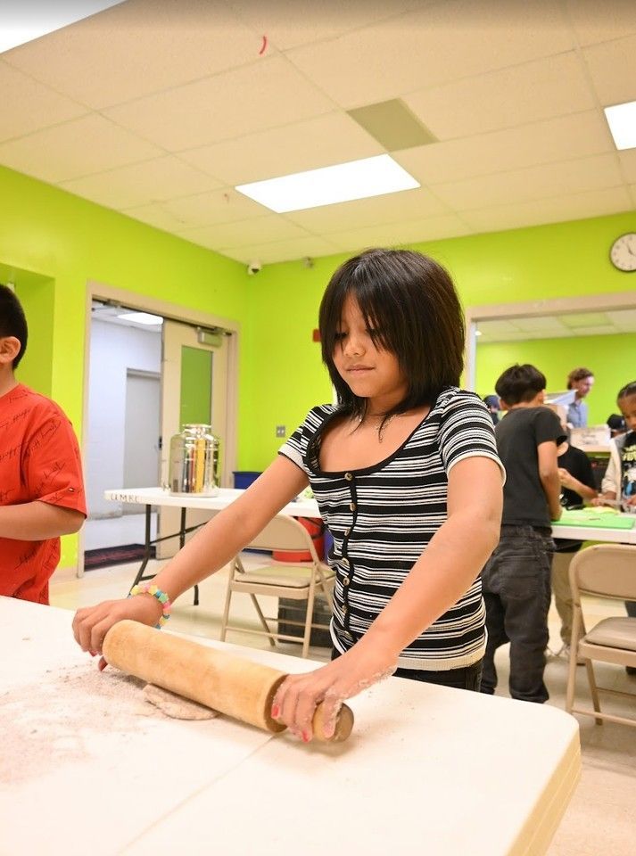 Child rolling dough on a table in a bright classroom kitchen