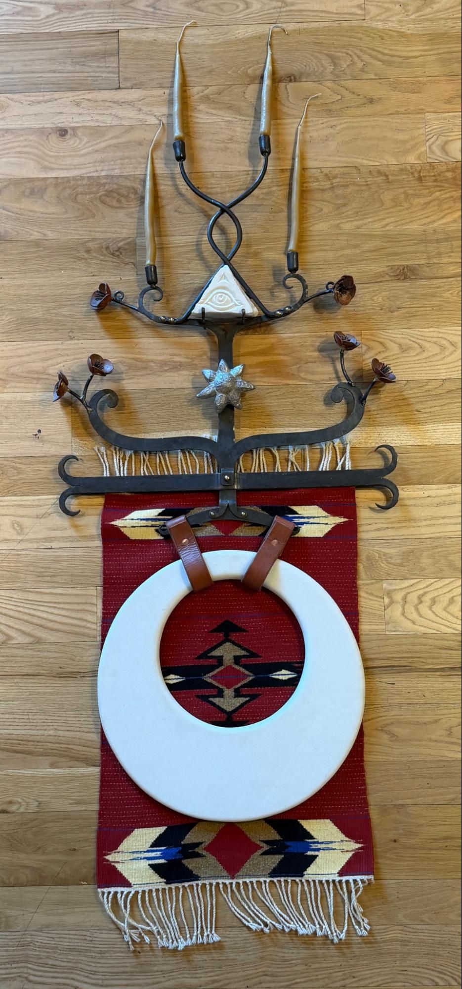 Decorative wall hanging with a white circular panel and red geometric center, framed by metal antlers on wood.
