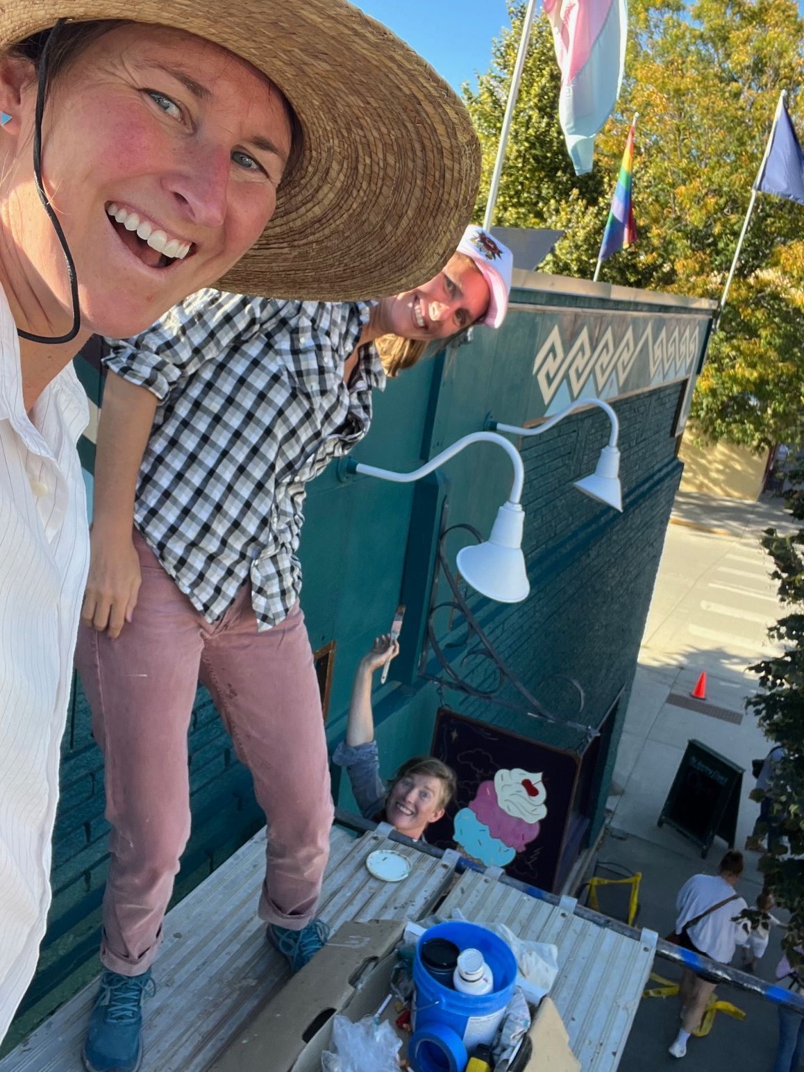 Smiling person in a straw hat leaning over a deck, with flags and a small decorated booth below.