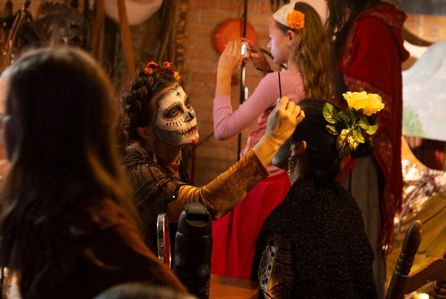 Costumed dancer with face paint kneels before a woman in a black dress at a festive event