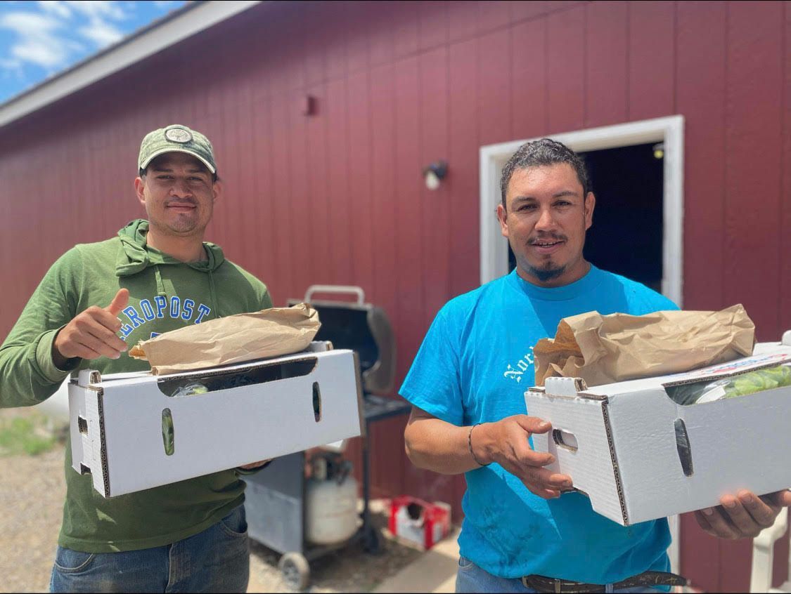 Two men holding white boxes of bread outside a red building