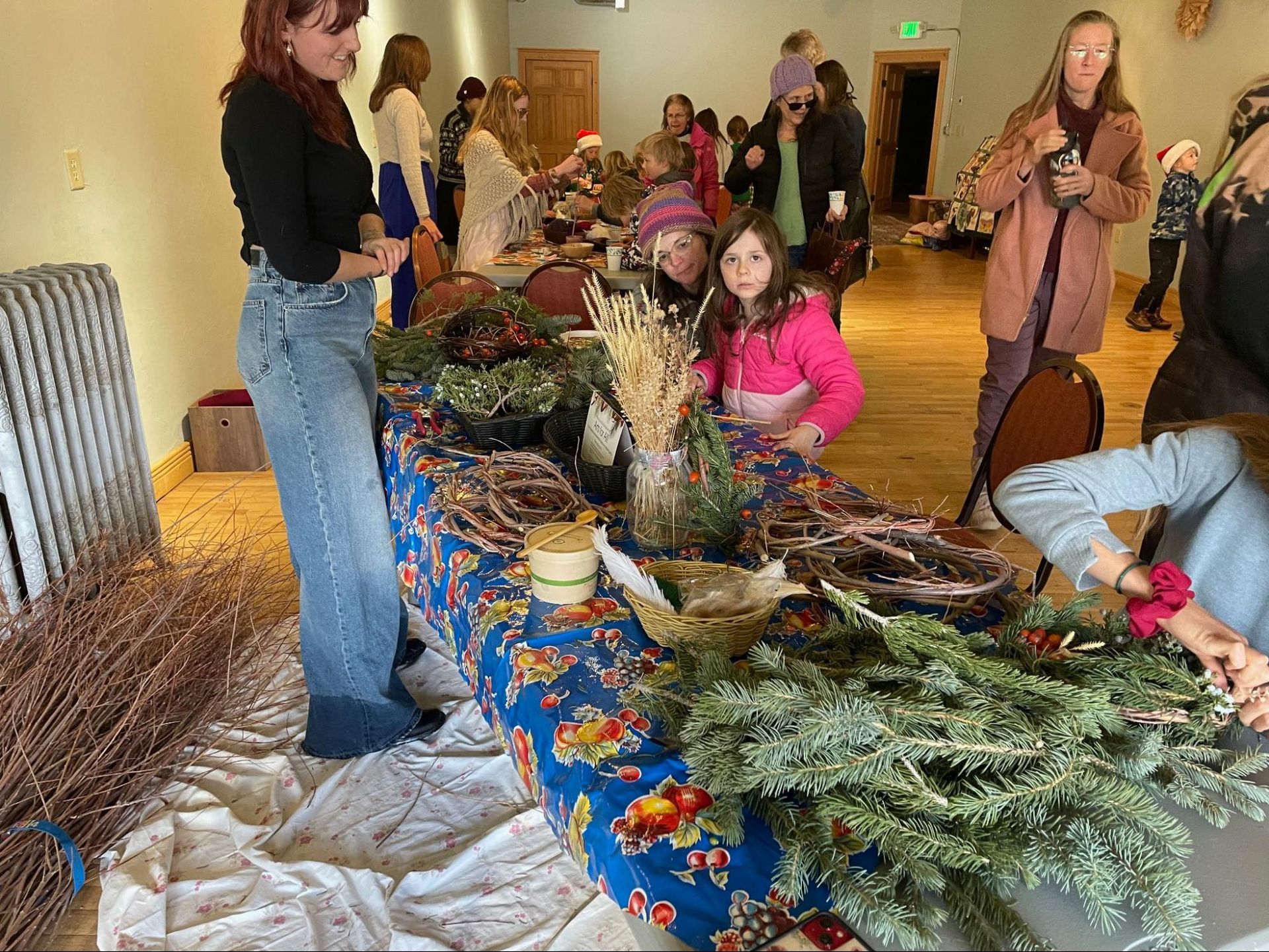 People browsing handmade wreaths and holiday decorations on a display table at an indoor market.