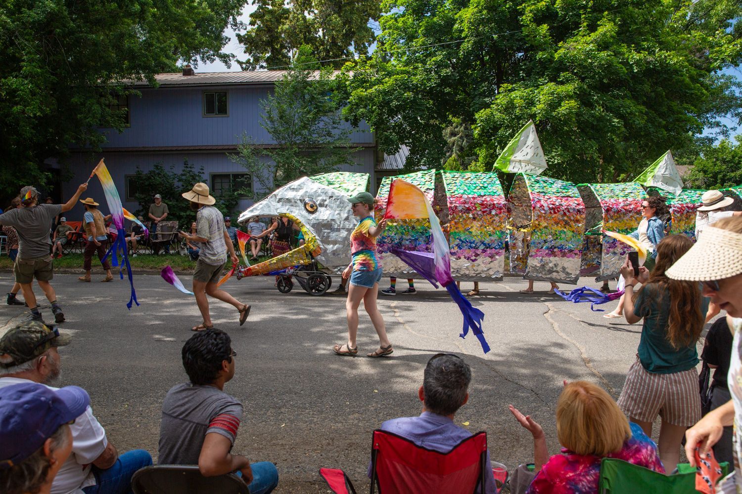Colorful parade dancers performing on a street while seated spectators watch under trees