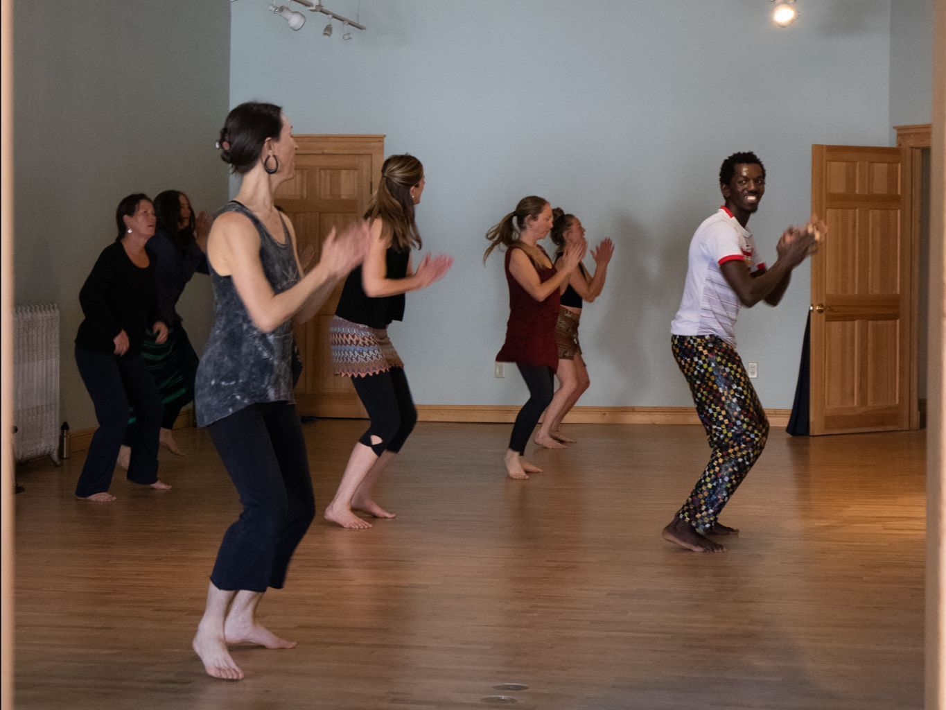 People dancing in a bright studio with wooden floors and doors