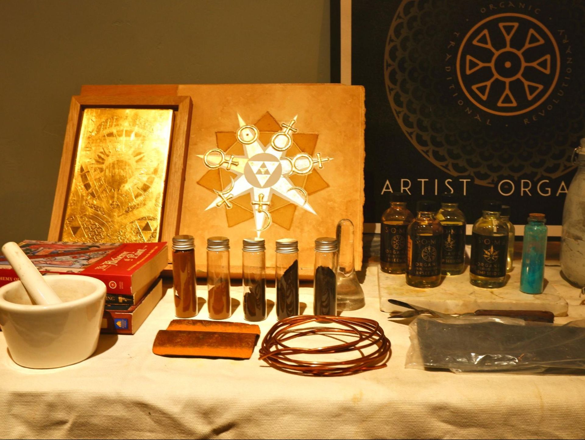 Art supplies displayed on a table with brushes, paint jars, palettes, and a framed artwork