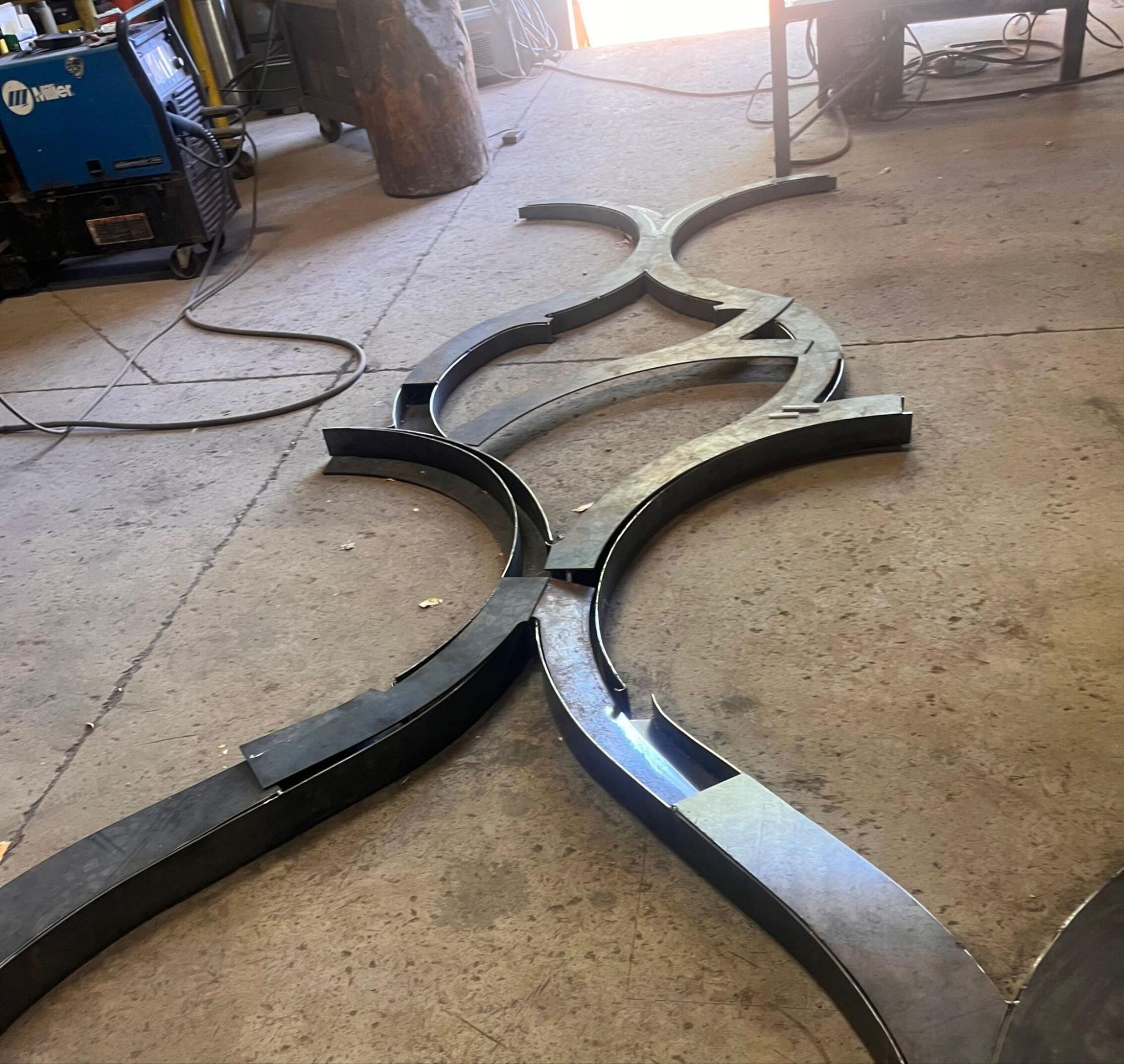 Curved black metal pieces arranged on a workshop floor, forming a decorative frame outline