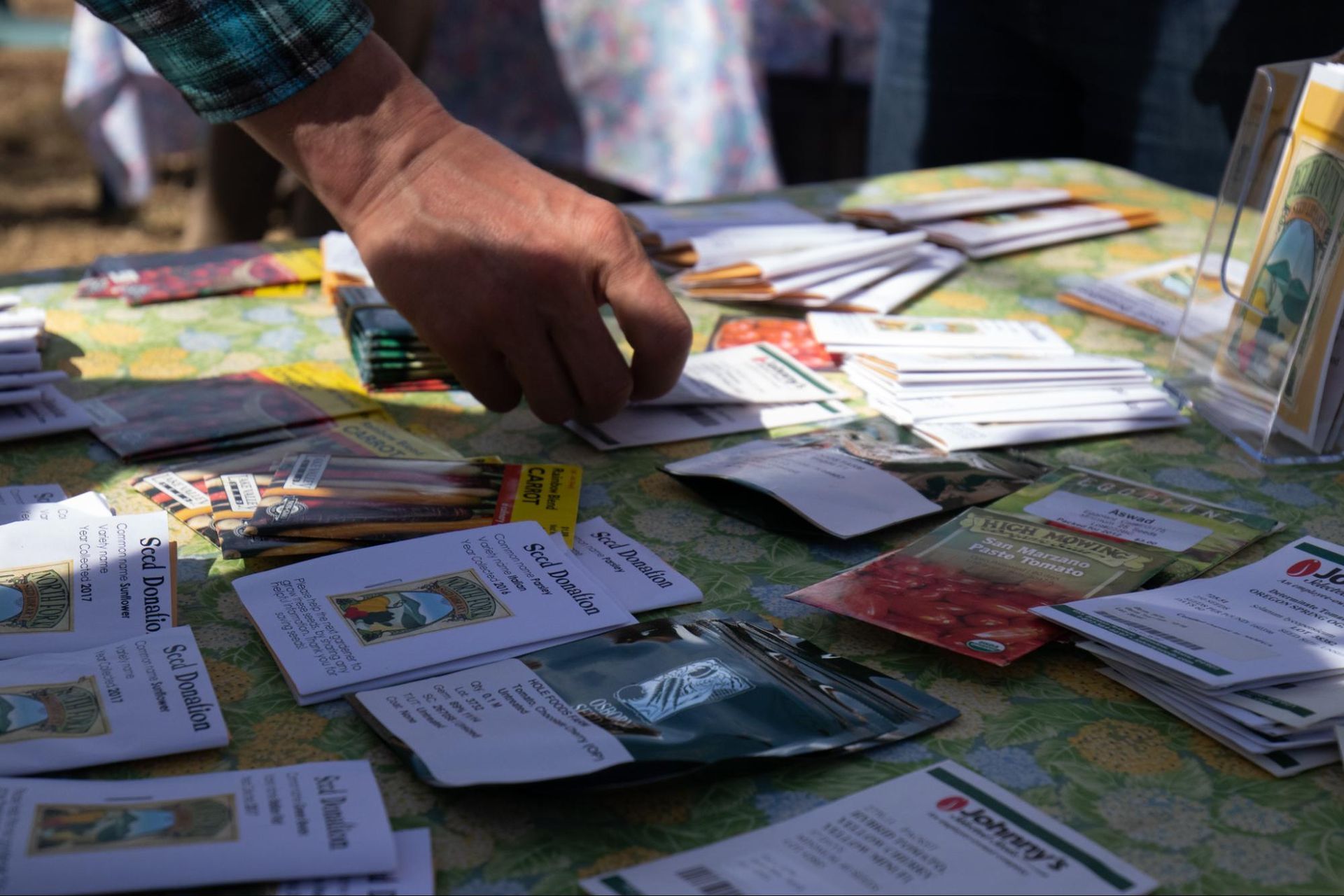 Hand reaching over a table covered with colorful cards and flyers at an outdoor market booth