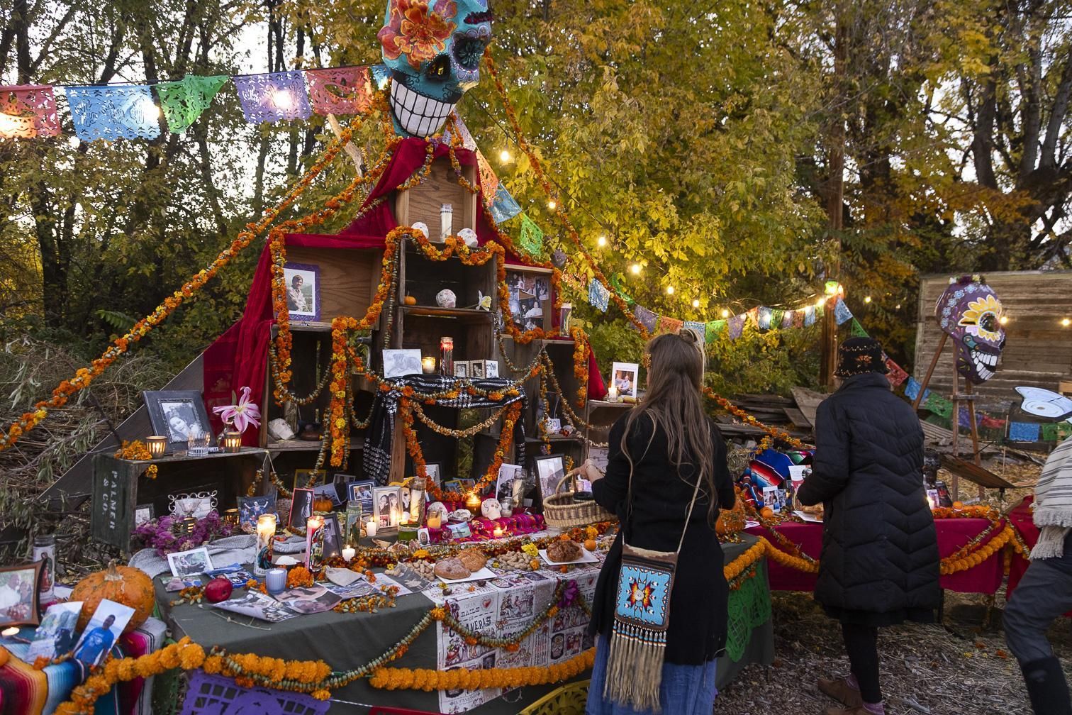 Outdoor altar decorated with marigolds, candles, and offerings; two people stand in a leafy garden at dusk