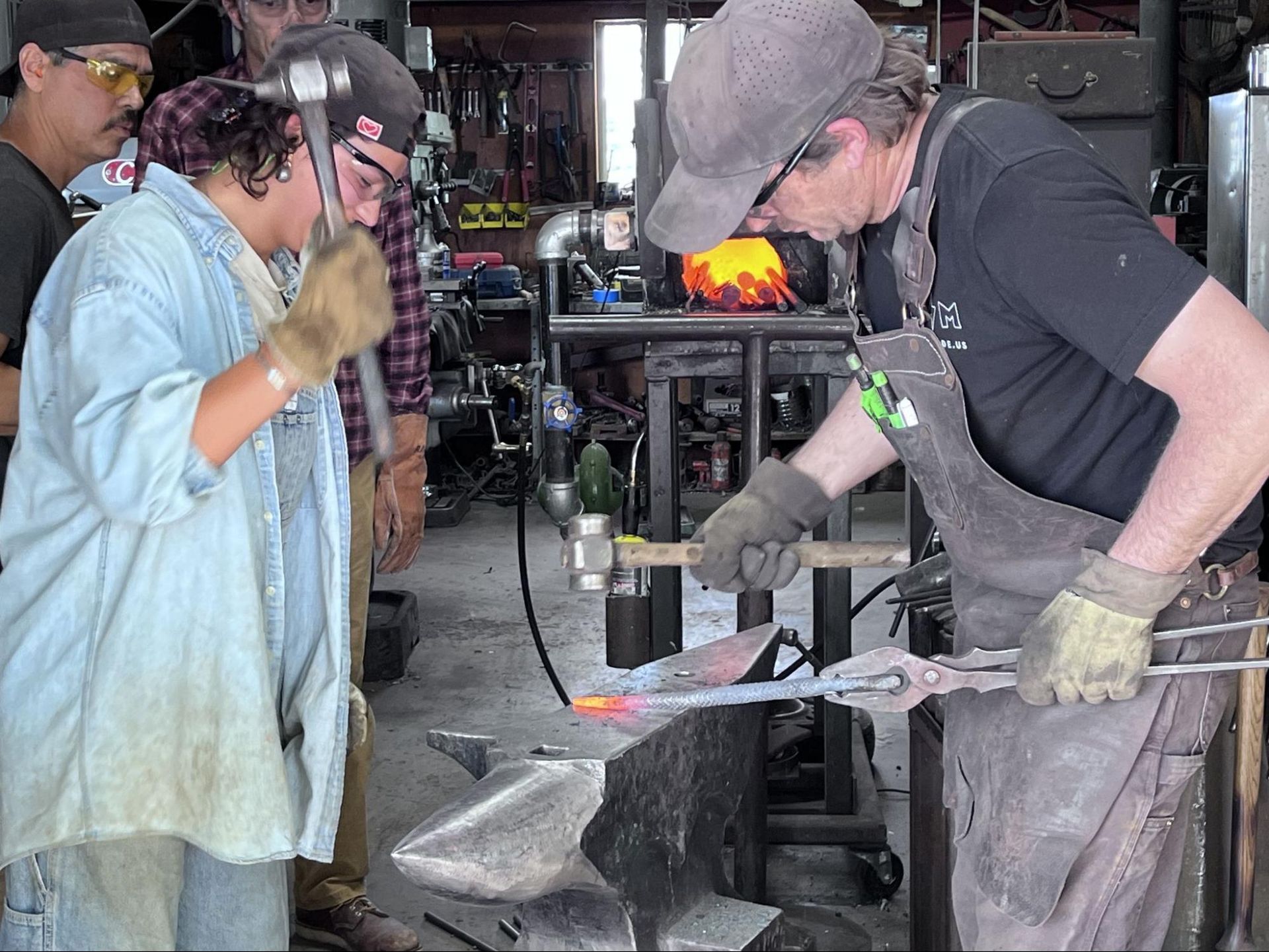 Two blacksmiths hammer red-hot metal on an anvil in a workshop.