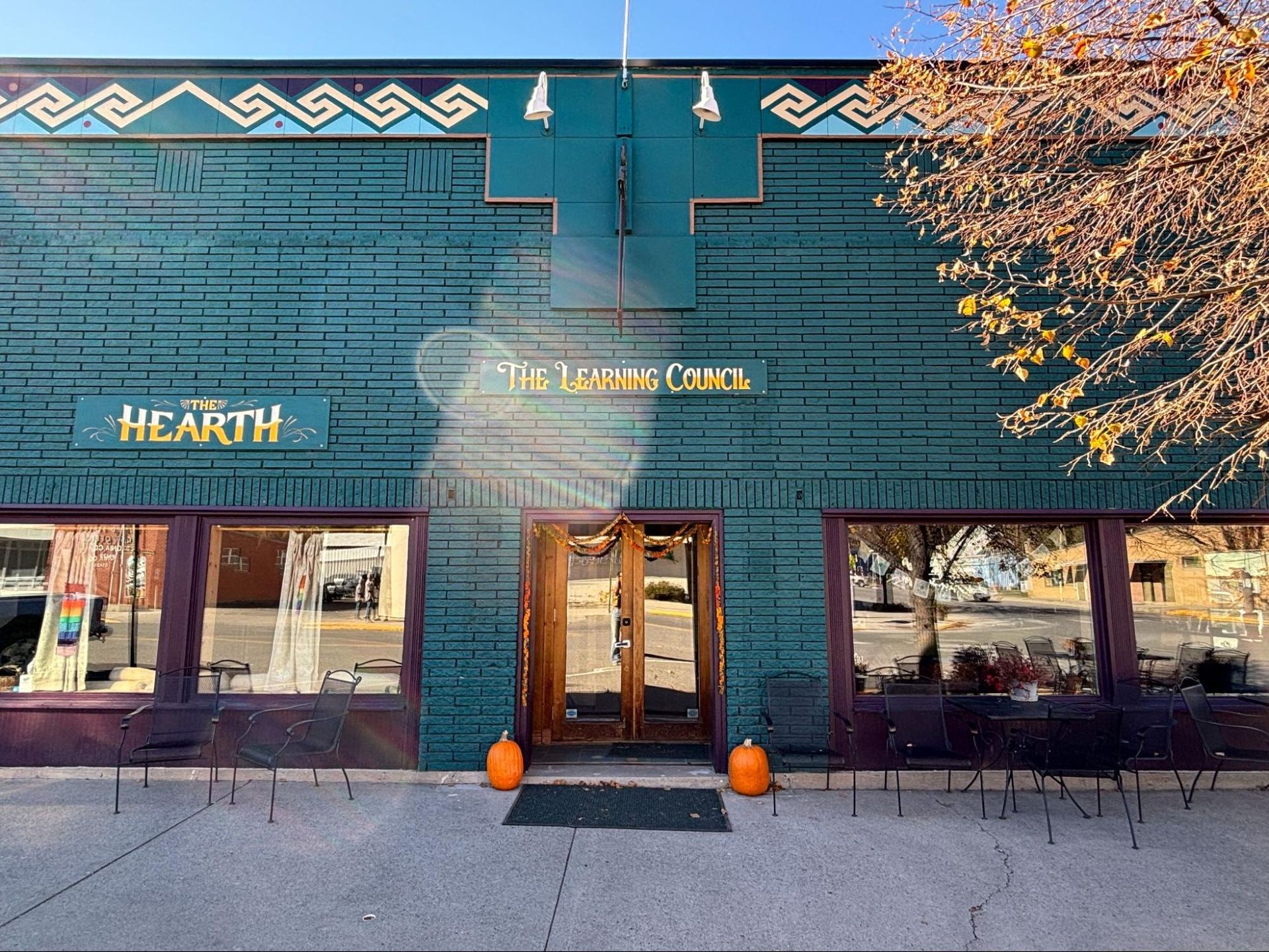 Storefront with teal facade, wooden doors, and gold sign reading “The Healing House” above a sidewalk café area