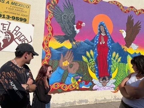 People painting a vibrant mural with blue birds, flowers, and a red-robed figure on a wall