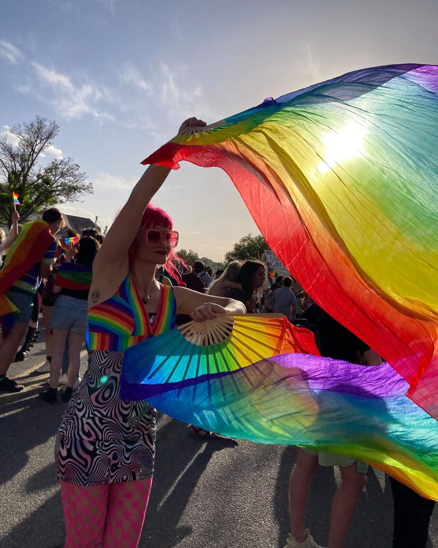 Person at a parade waving rainbow fabric in bright sunlight