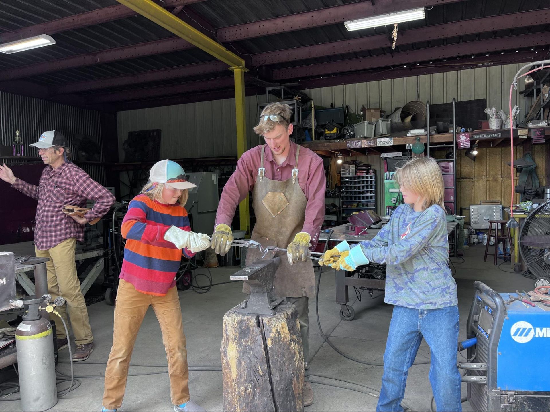 People forging metal in a workshop, with three workers hammering at an anvil.