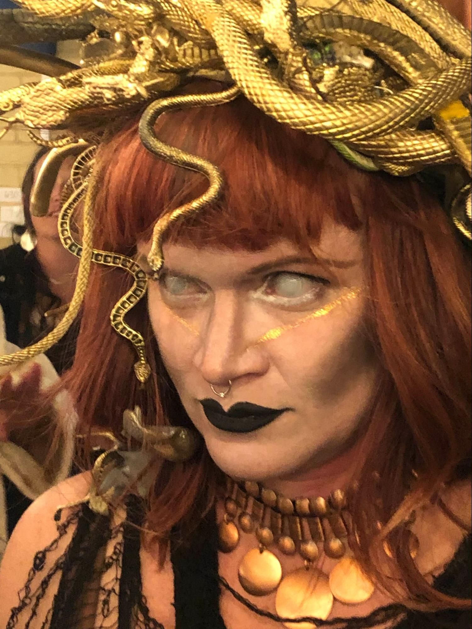 Close-up of a woman with red hair and black lipstick in ornate gold Medusa-style costume