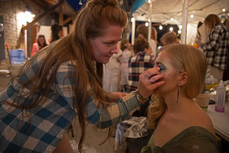 Woman applying makeup to another woman backstage in a dressing room