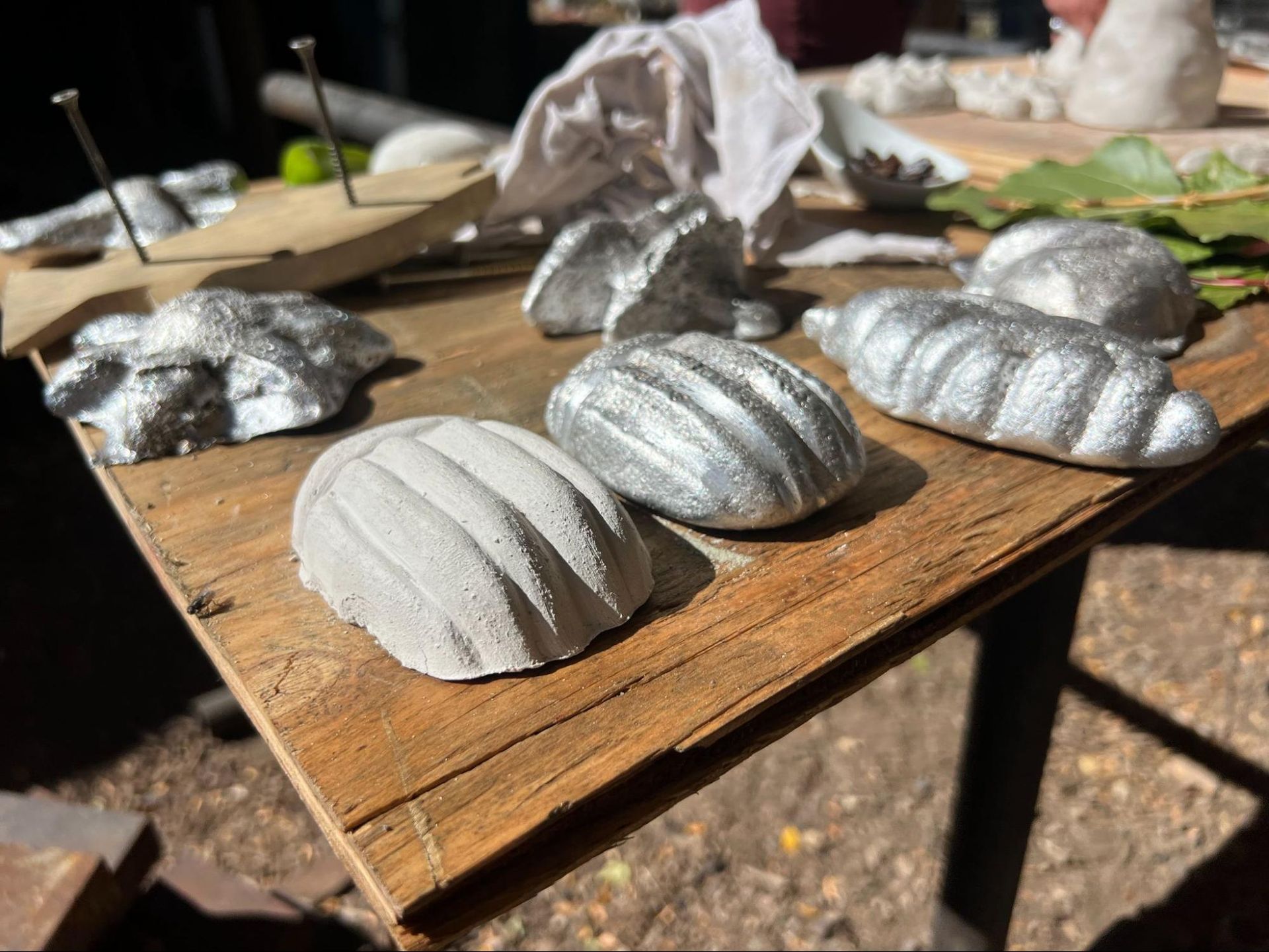 Silver-painted shell-shaped crafts drying on a wooden board outdoors