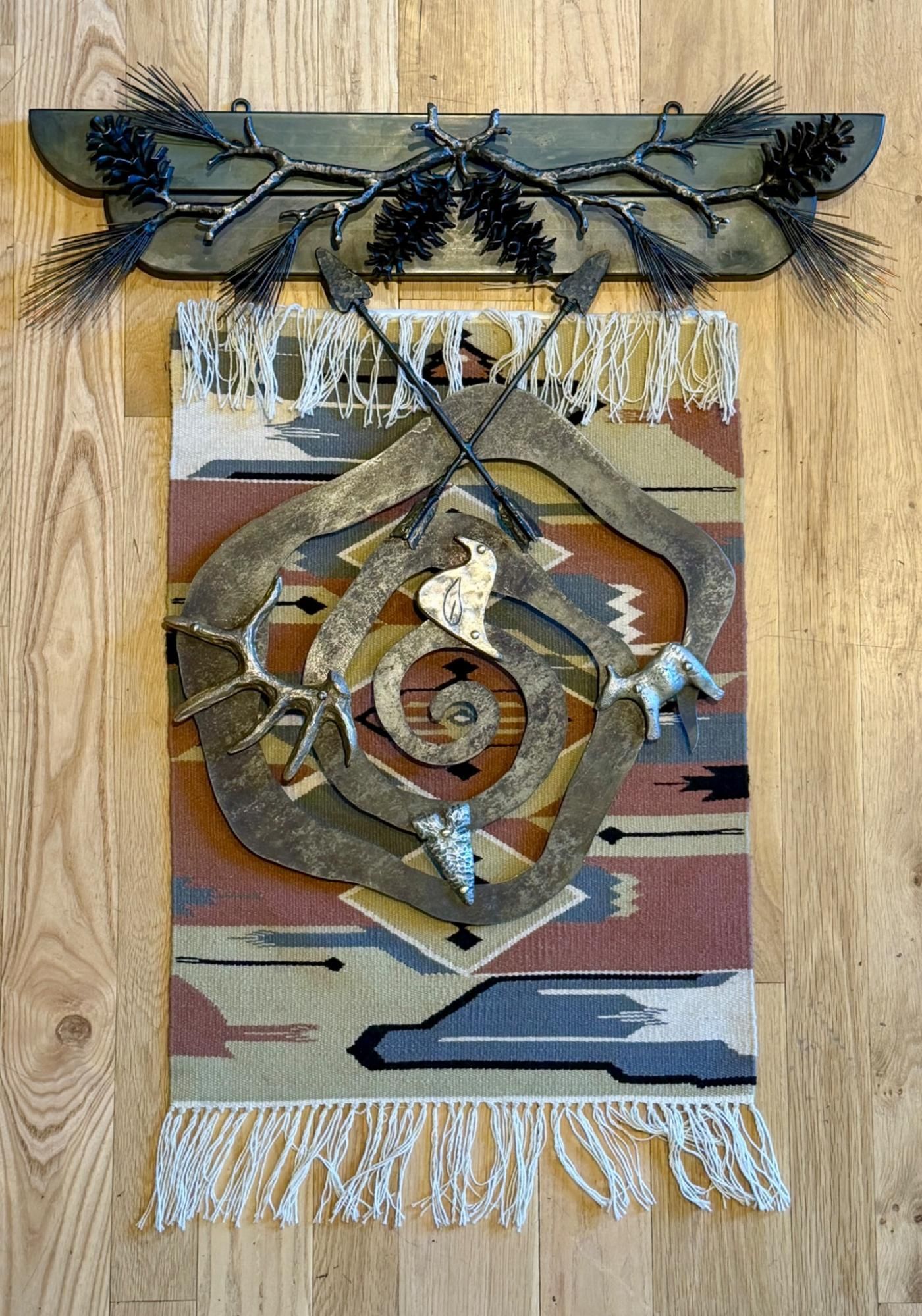 Decorative woven wall hanging with a carved spiral motif, feathers, and fringe on a wooden background