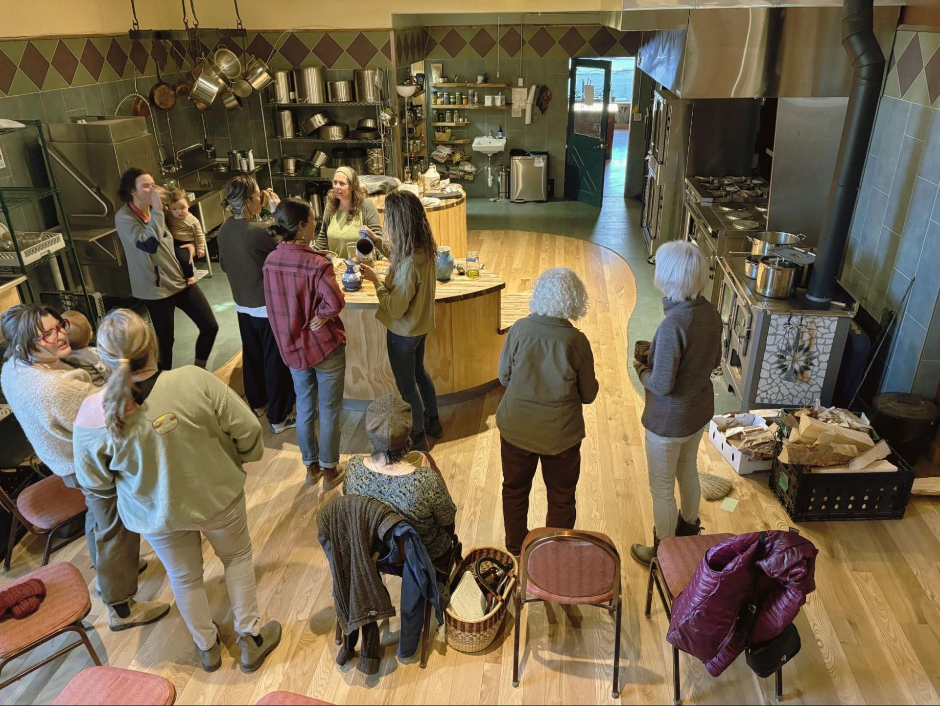 People gathered around a counter in a cozy café, chatting and standing near tables and chairs.