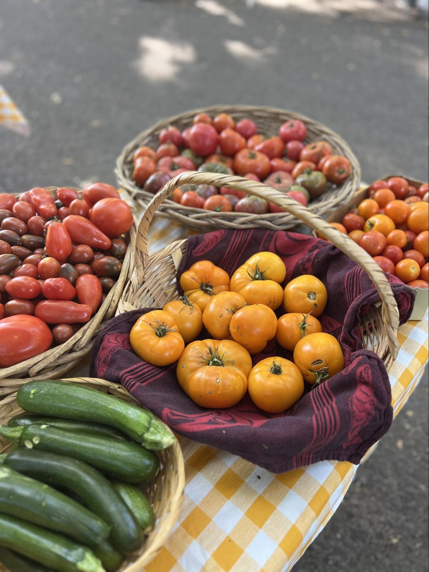 Baskets of tomatoes, cucumbers, and peppers on a market stall with a checkered cloth