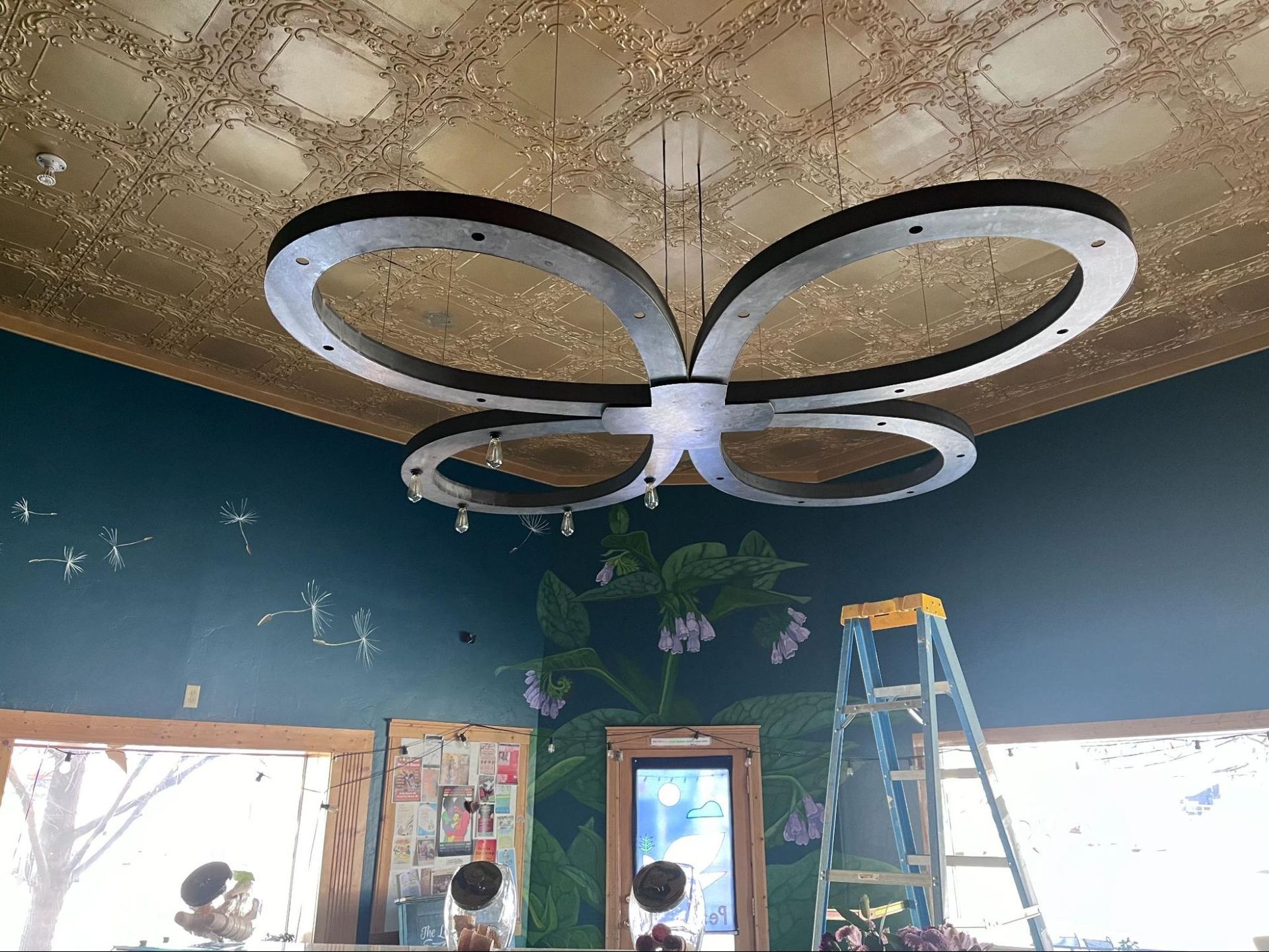 Children in a classroom with butterfly ceiling lights, blue walls, a window, and a ladder near the corner