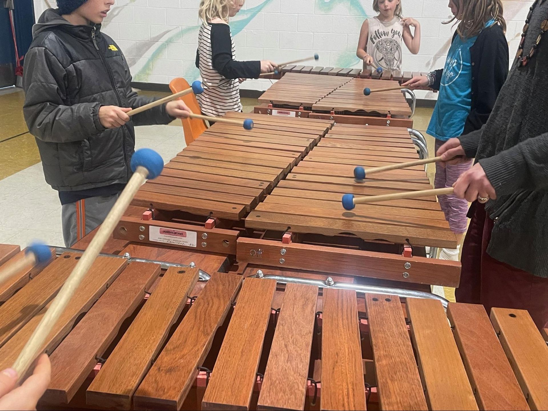 People playing a wooden xylophone outdoors, striking bars with mallets.