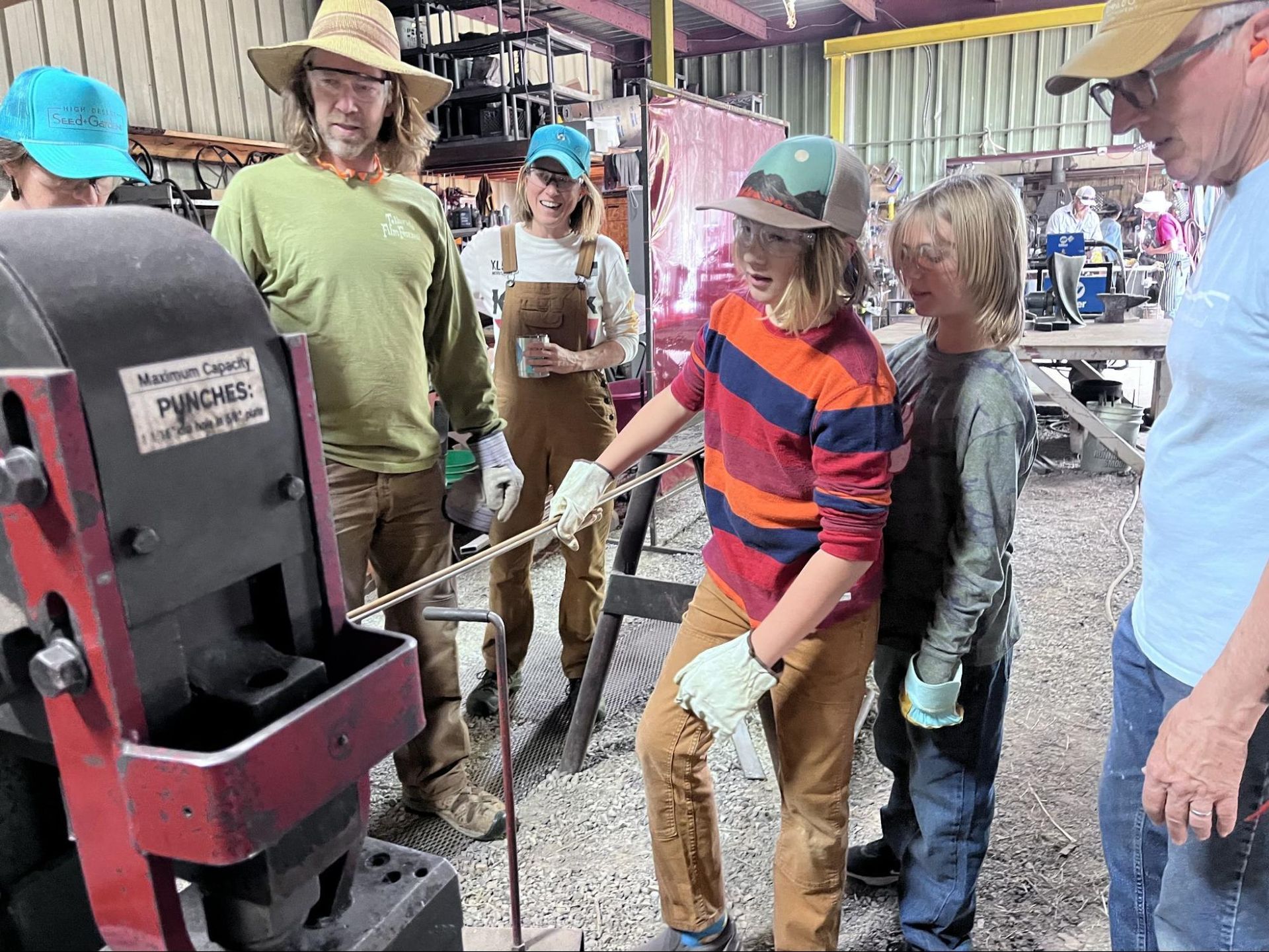 People gathered around a red machine as a woman in a striped shirt operates it with a long tool.