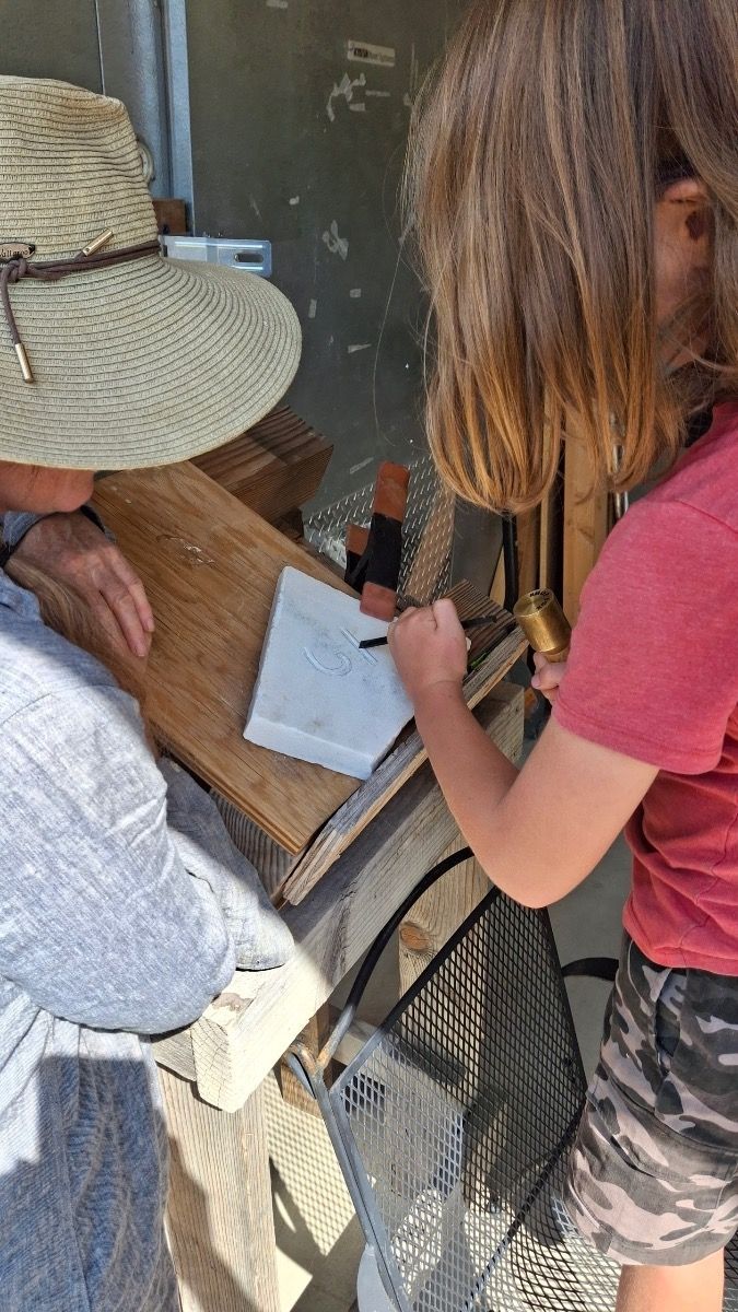 Two people leaning over a table, writing on a clipboard beside a window in a rustic setting