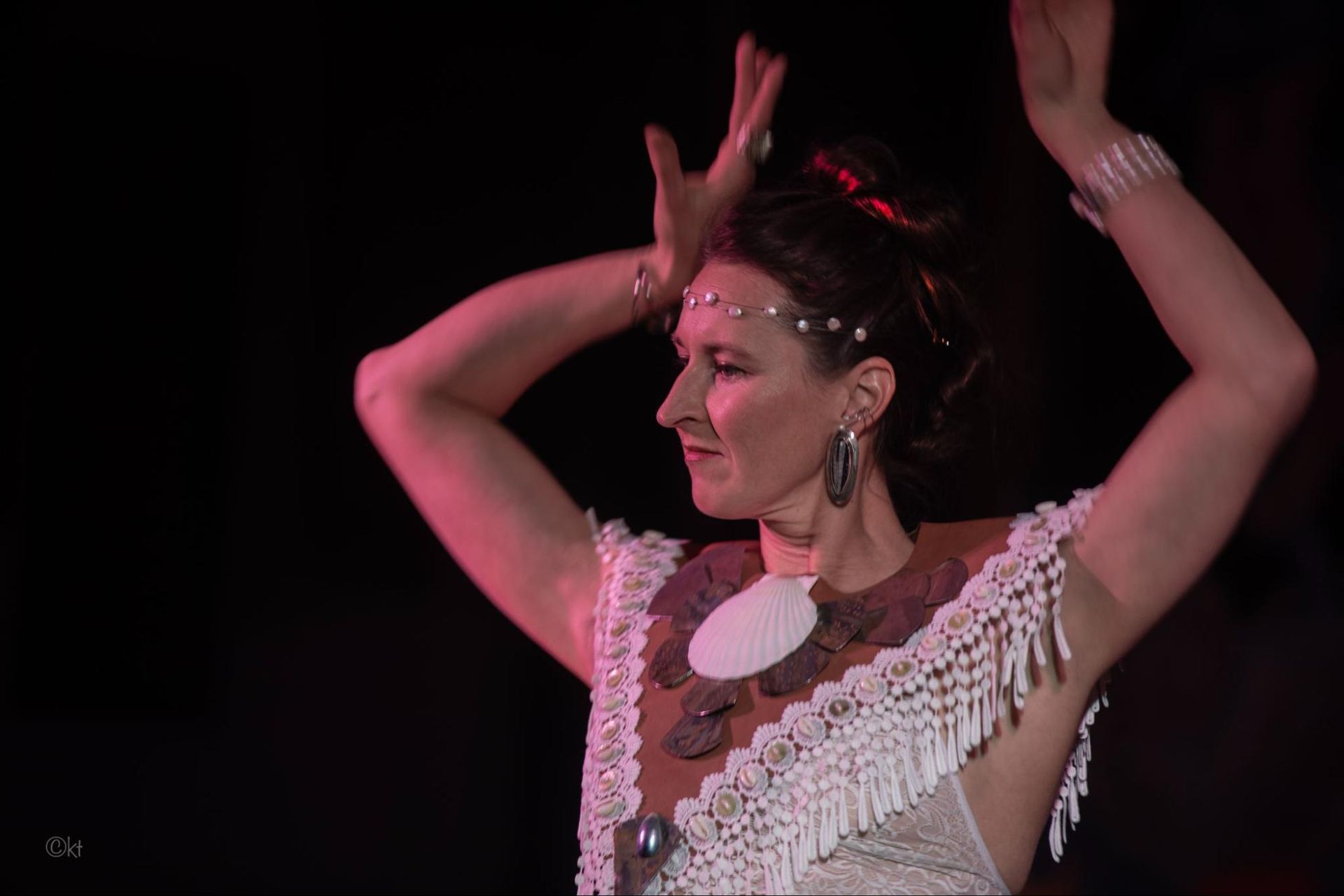 Dancer in a white fringed costume with arms raised under pink stage lighting