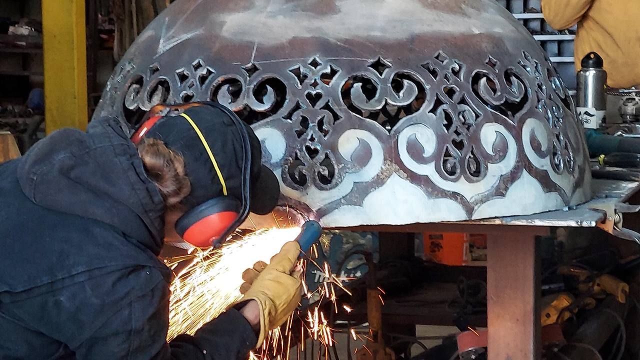 Worker in protective gear welding a decorative metal panel, with sparks flying in a workshop