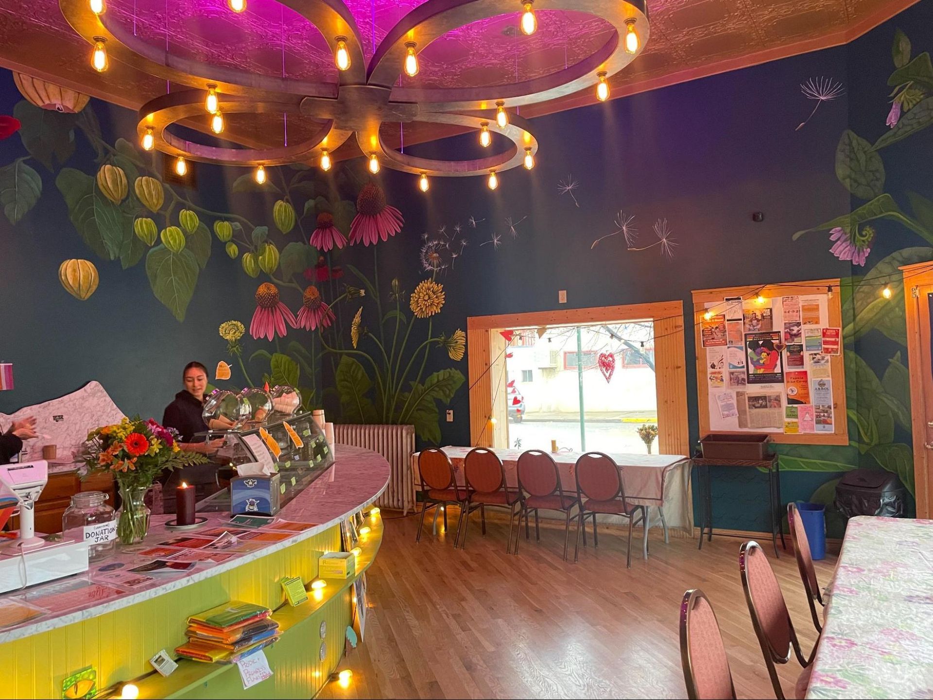 Colorful cafe interior with a curved counter, floral wall decor, and warm hanging lights