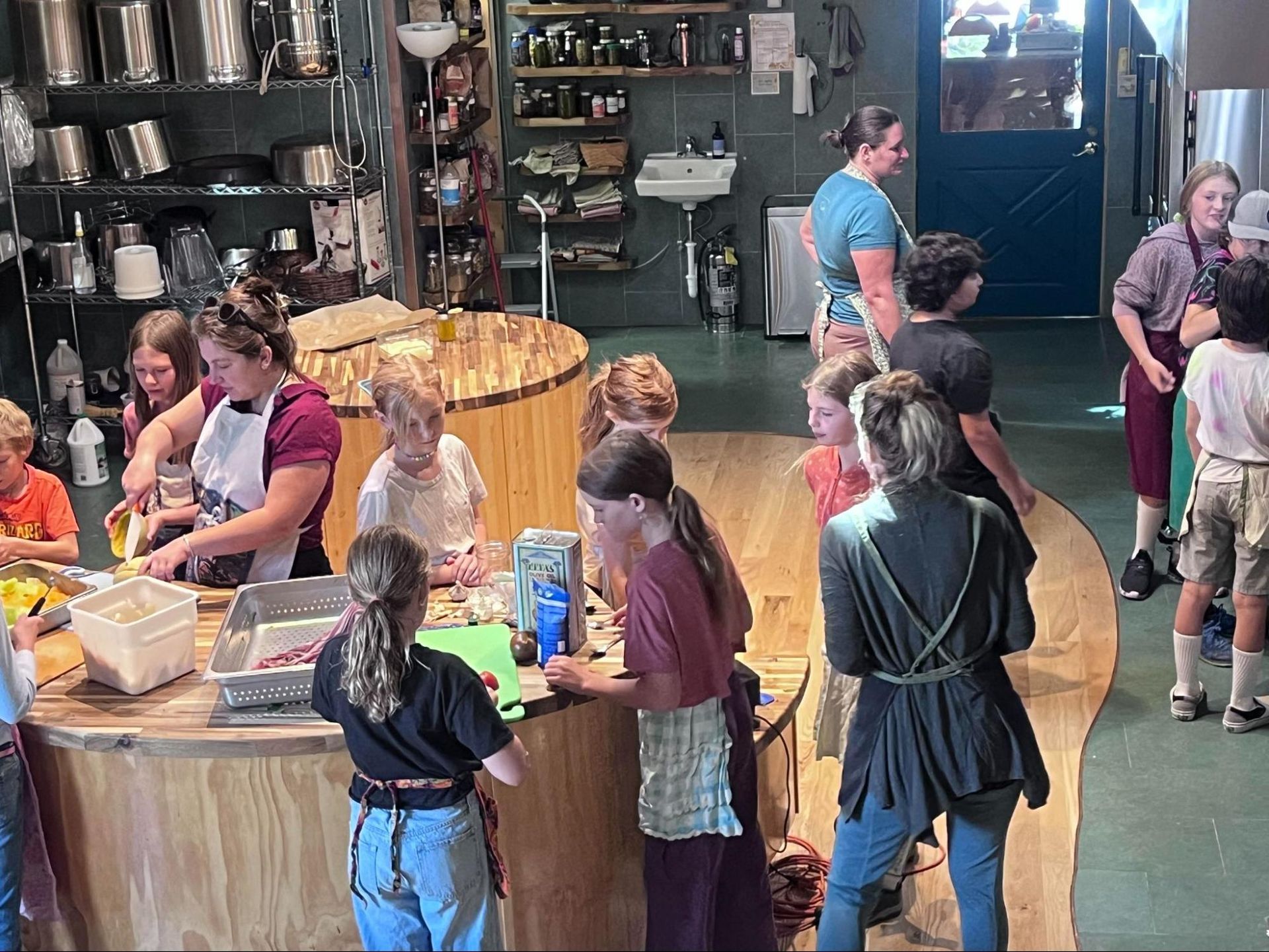 People gathered around a communal table in a kitchen or café, talking and eating food.