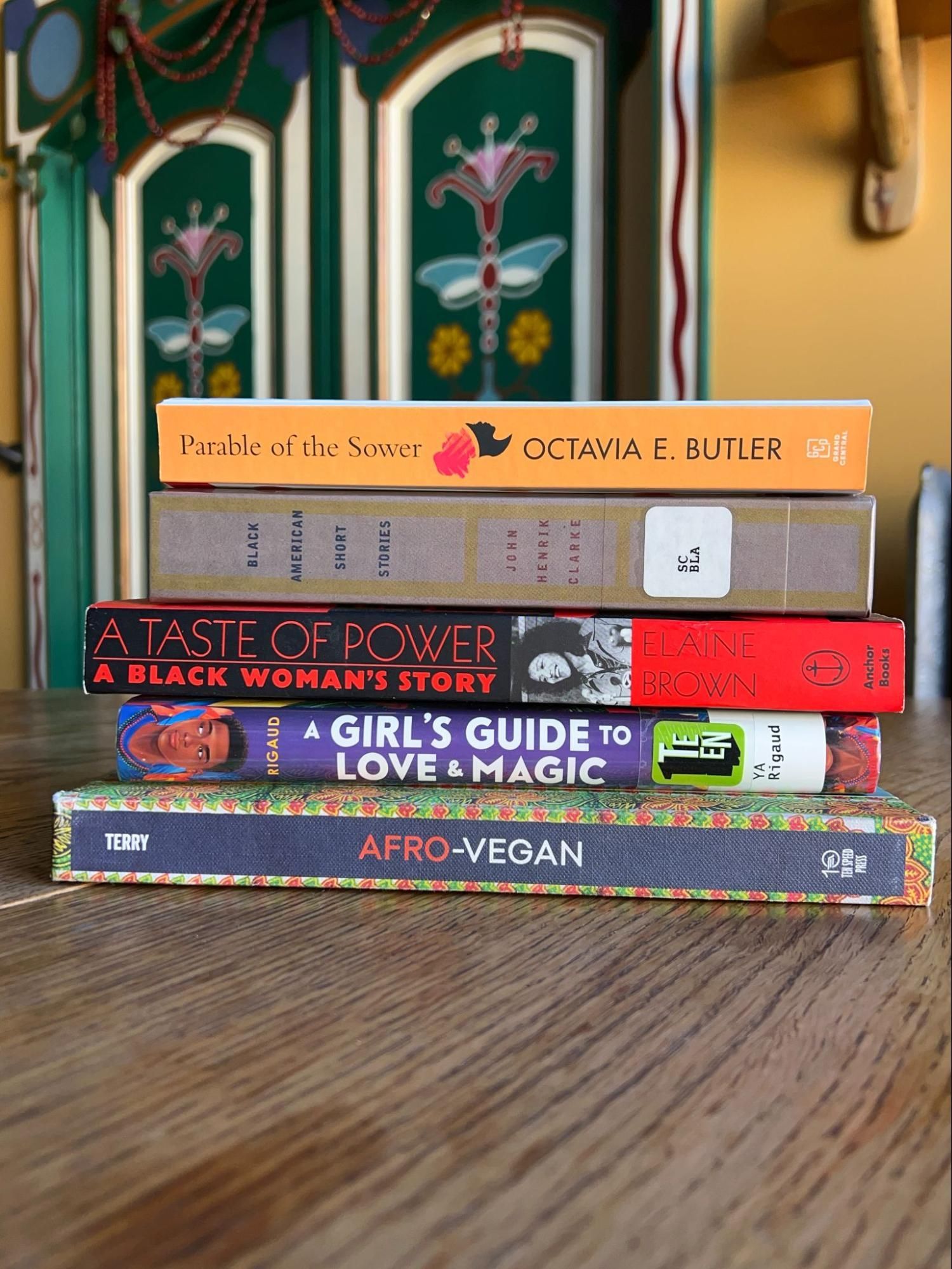 Stack of colorful books on a wooden table in front of a patterned wall.
