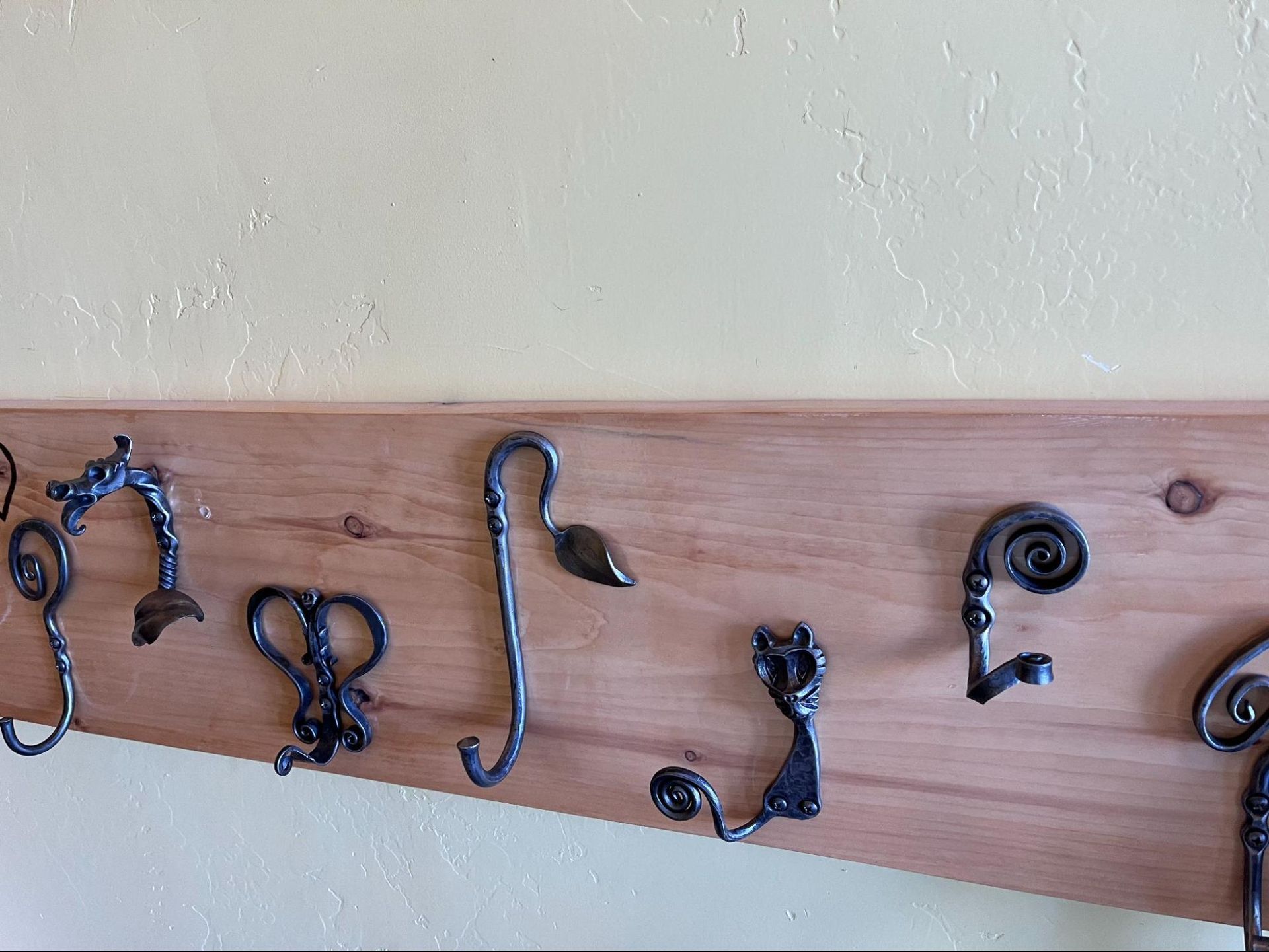 Decorative metal wall hooks mounted on a wooden plank against a white wall.