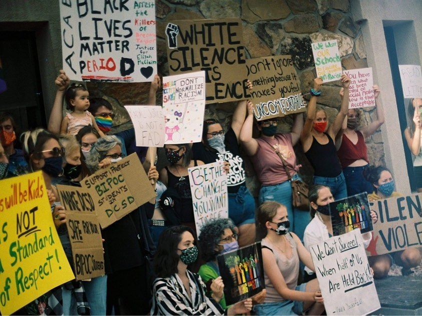 Masked protesters holding signs at a Black Lives Matter demonstration outside a building.