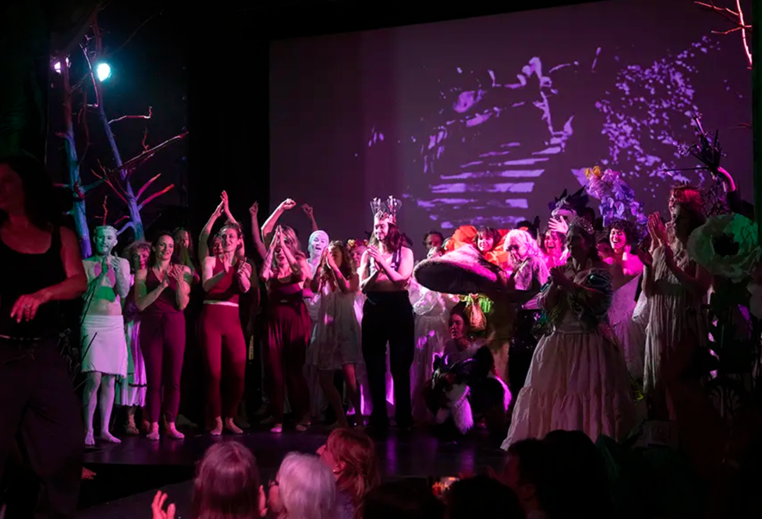 Crowd dancing on a dim stage under pink and purple lights with a projected abstract background
