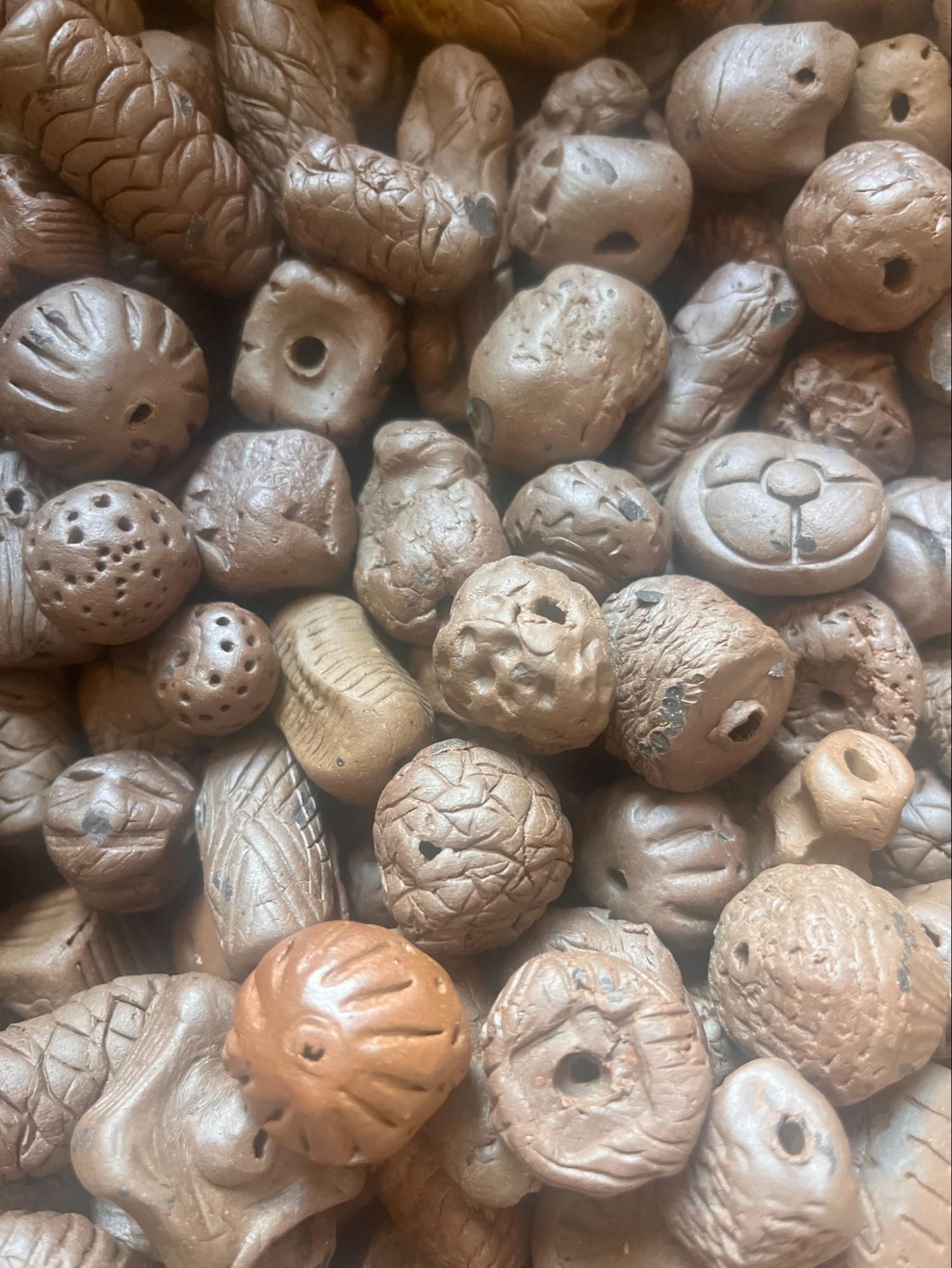 Assorted small carved brown nuts or seed pods with holes, arranged in a close-up pattern