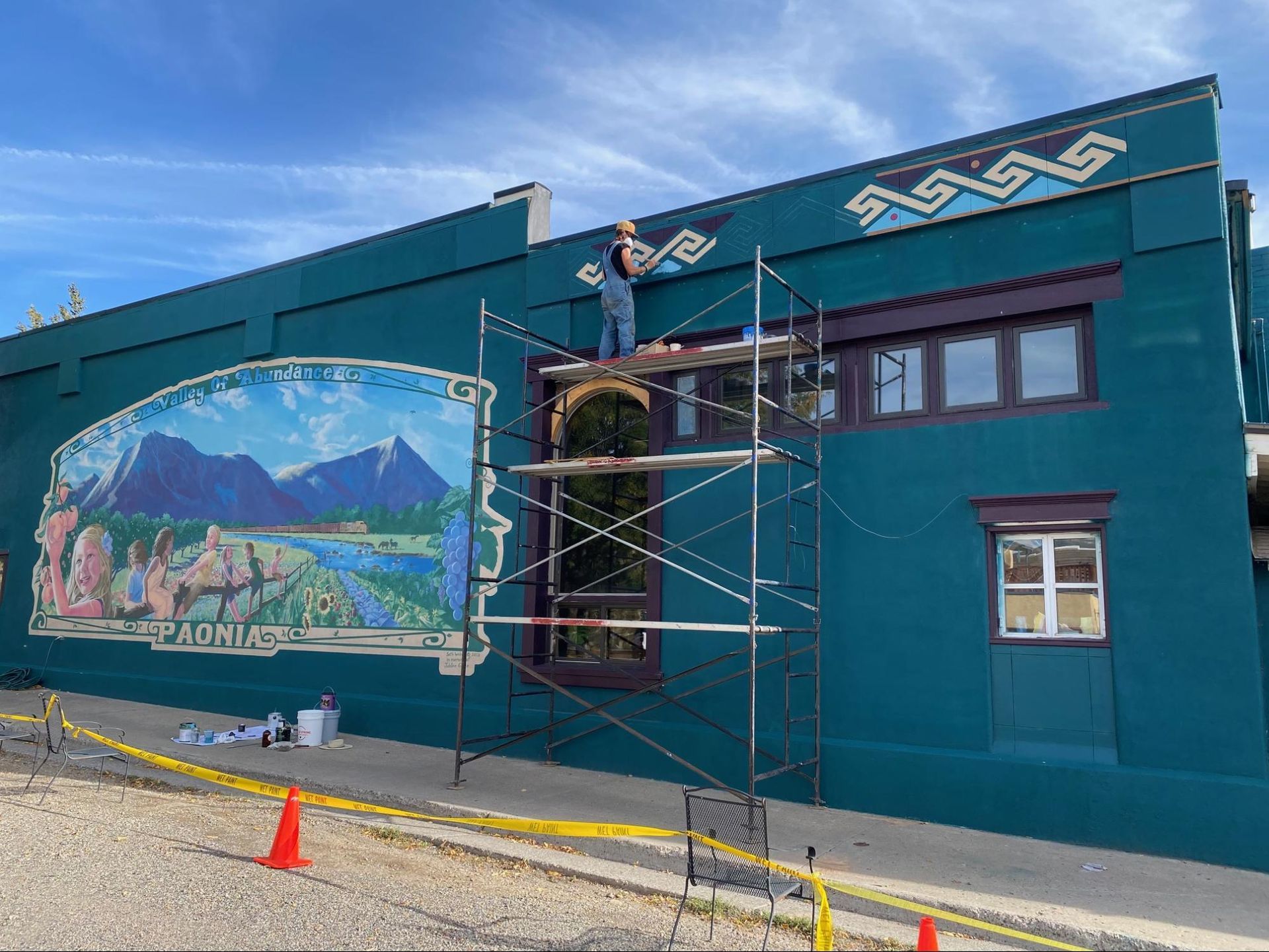 Teal building with mural and scaffolding, under renovation on a sunny street.