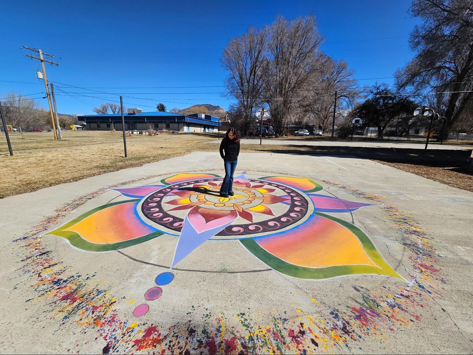 Person standing on a colorful circular street mural in a sunny park-like open area