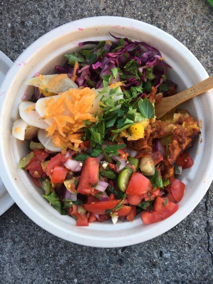 A bowl of colorful salad with tomato, shredded carrot, red cabbage, greens, and dressing on a stone surface