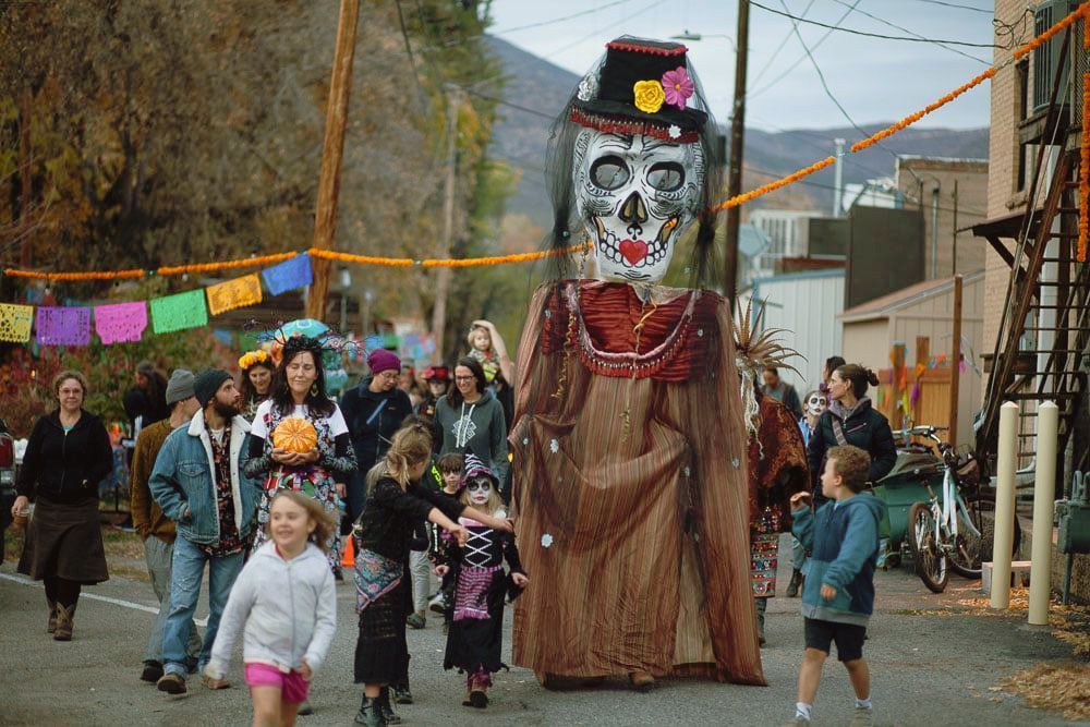 Festival parade with a giant skull figure and children walking down a decorated street