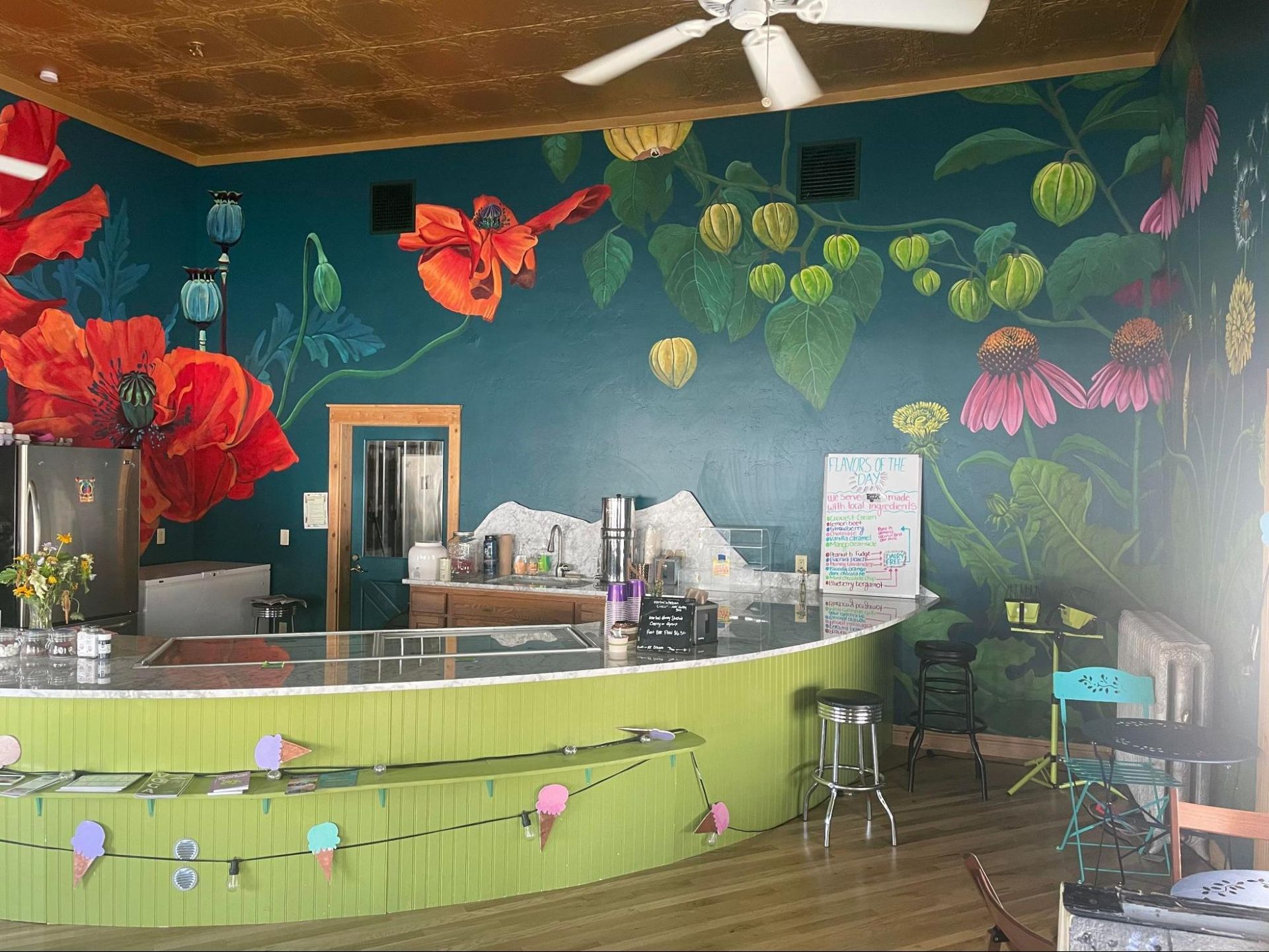 Colorful café counter with green front, red flower decor, and hanging lanterns in a tropical-themed room