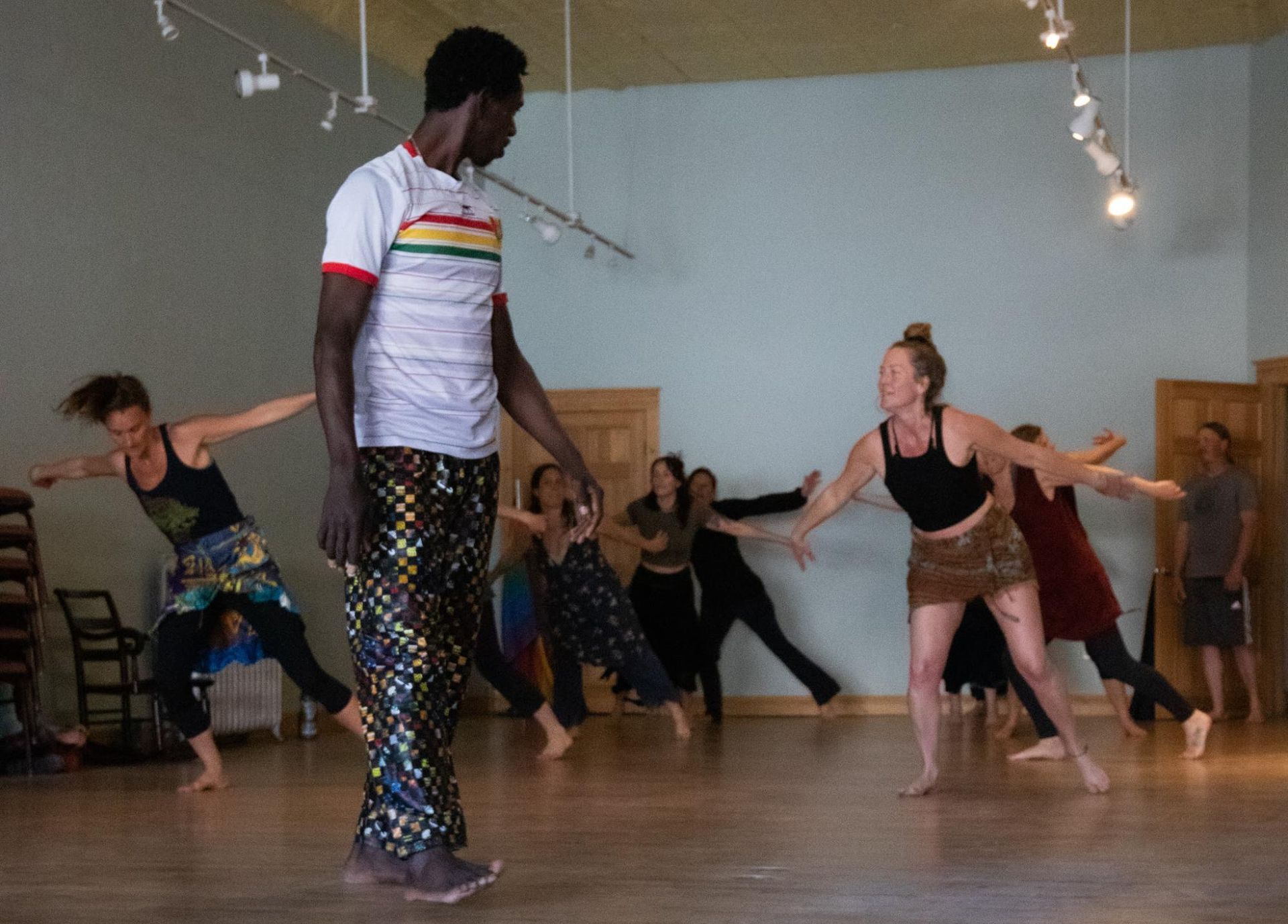 People dancing in a studio, with a man in a rainbow-striped shirt in the foreground