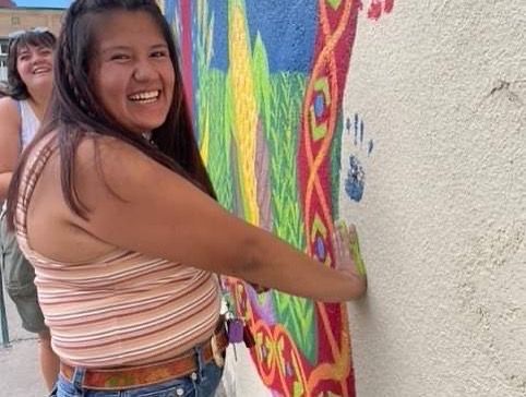 Woman smiling while painting a colorful mural on a wall outdoors