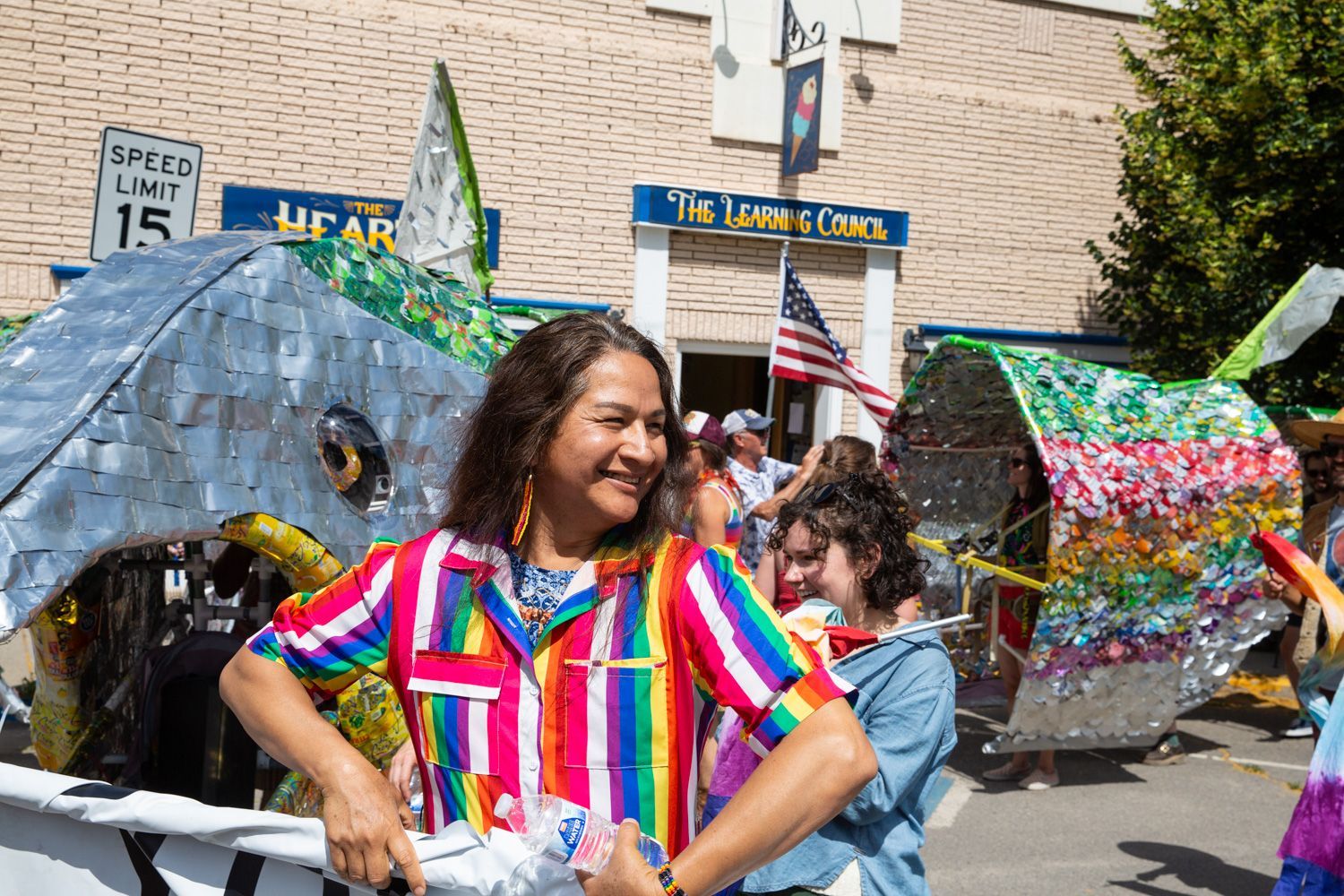People smiling in colorful costumes during a street parade in front of a building