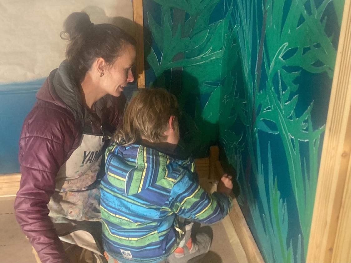 Two people painting a large blue-green mural on a wall.
