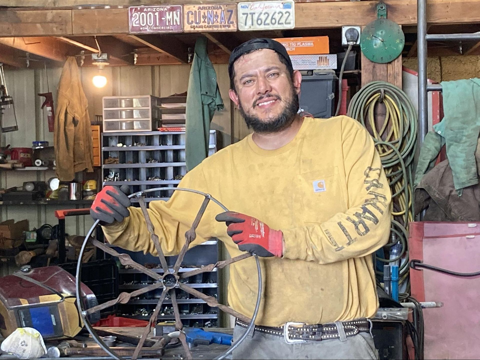Man in yellow shirt holding cables in a cluttered garage workshop