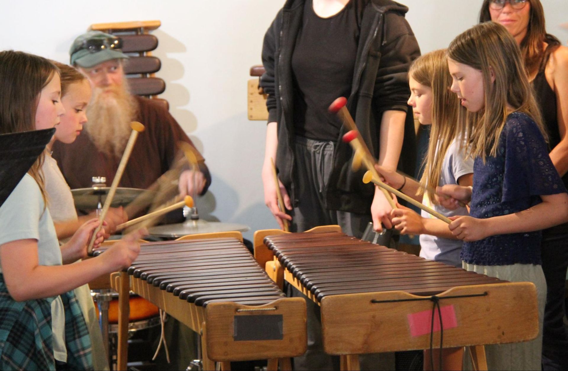 Children playing xylophones in a music classroom with an adult instructor nearby