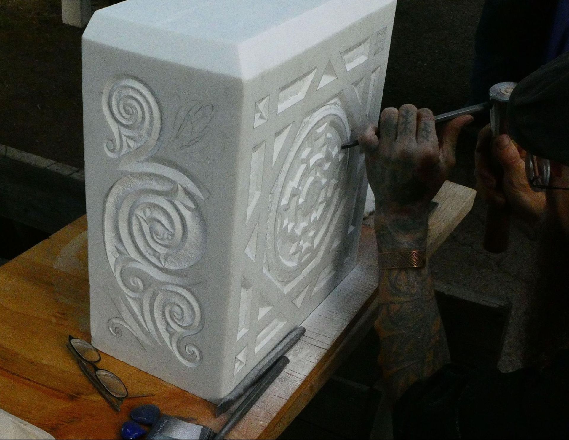 White decorative stone slab with spiral carvings, being worked on by hands in a workshop or studio