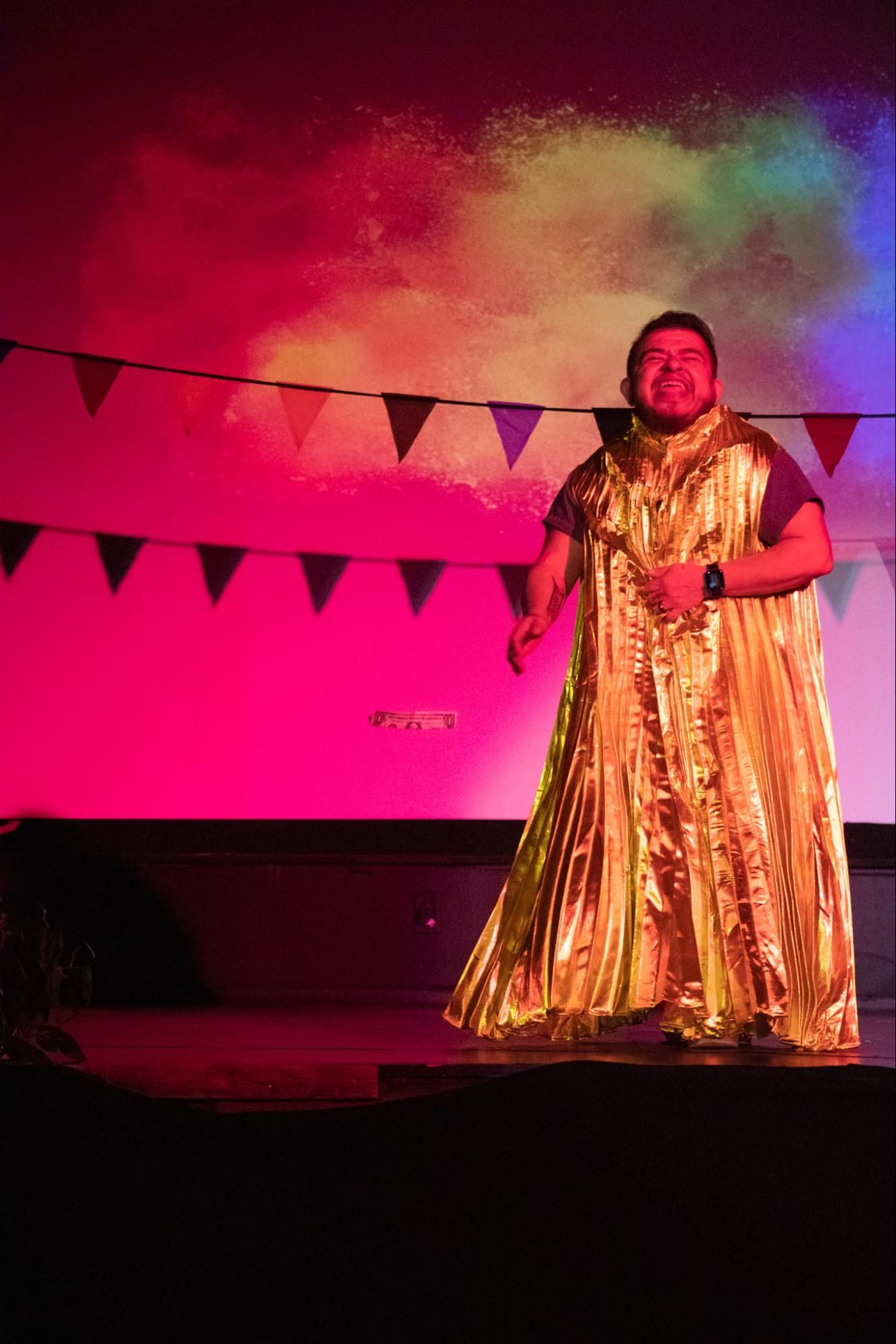 Person in a gold gown on a lit stage with pink and green lighting and bunting banners