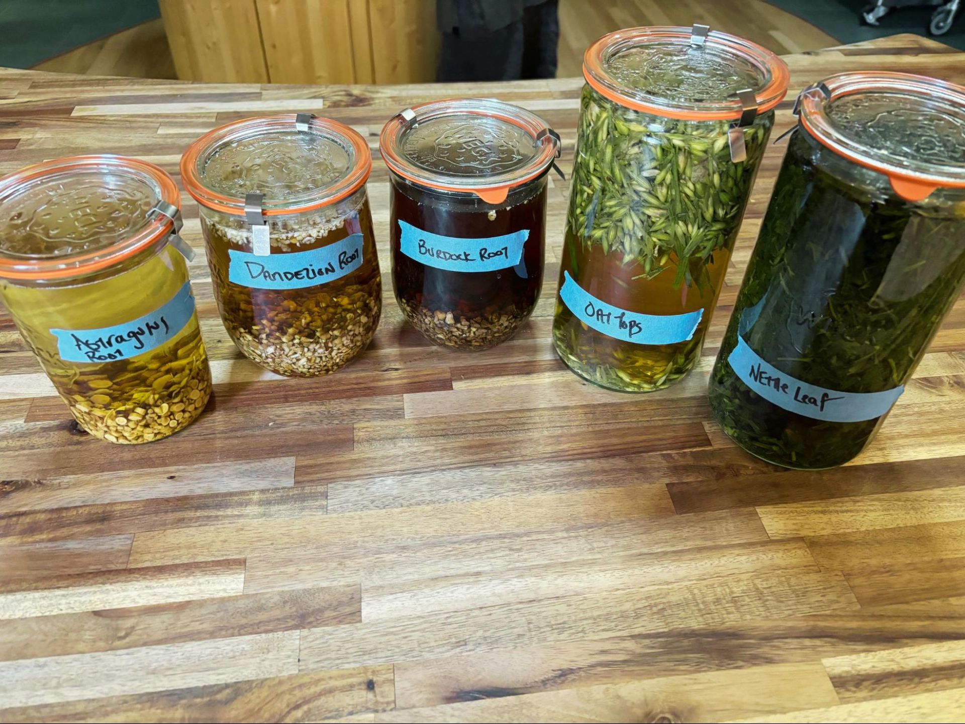 Five labeled jars of herbs and spices lined up on a wooden countertop.